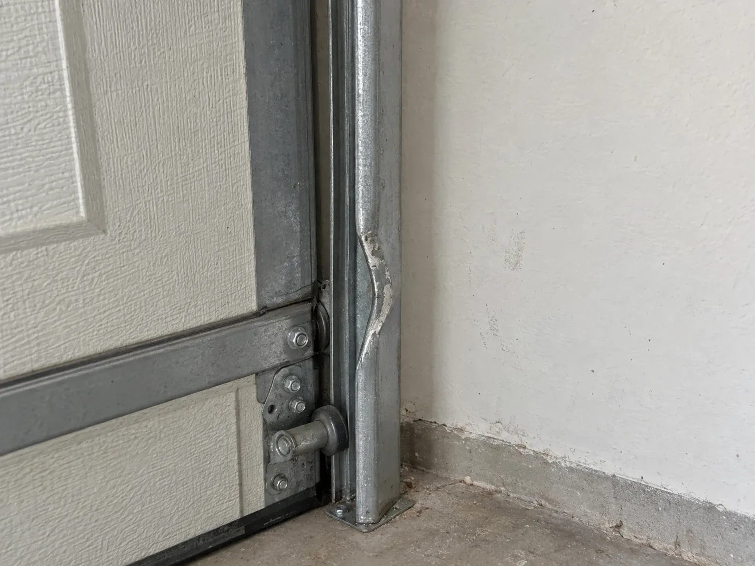 A garage door track kinked inward, its lip bent so the roller cannot pass