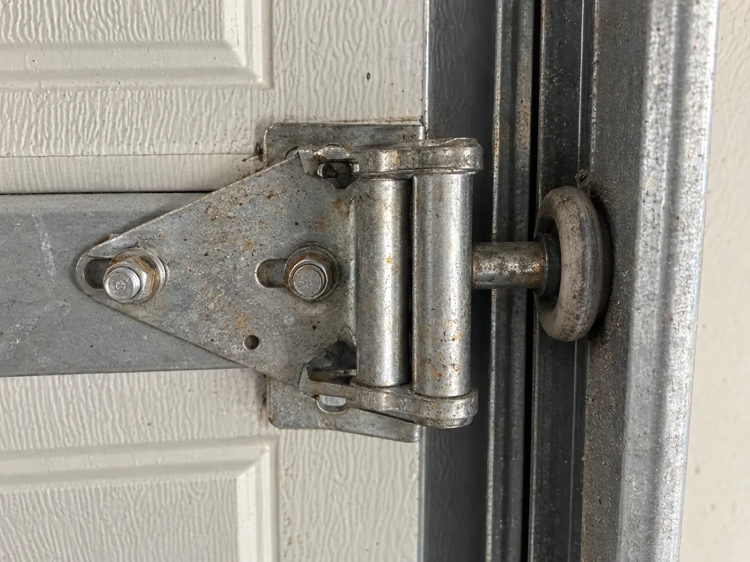 A worn garage door roller, flat on one side, beside its hinge in the track