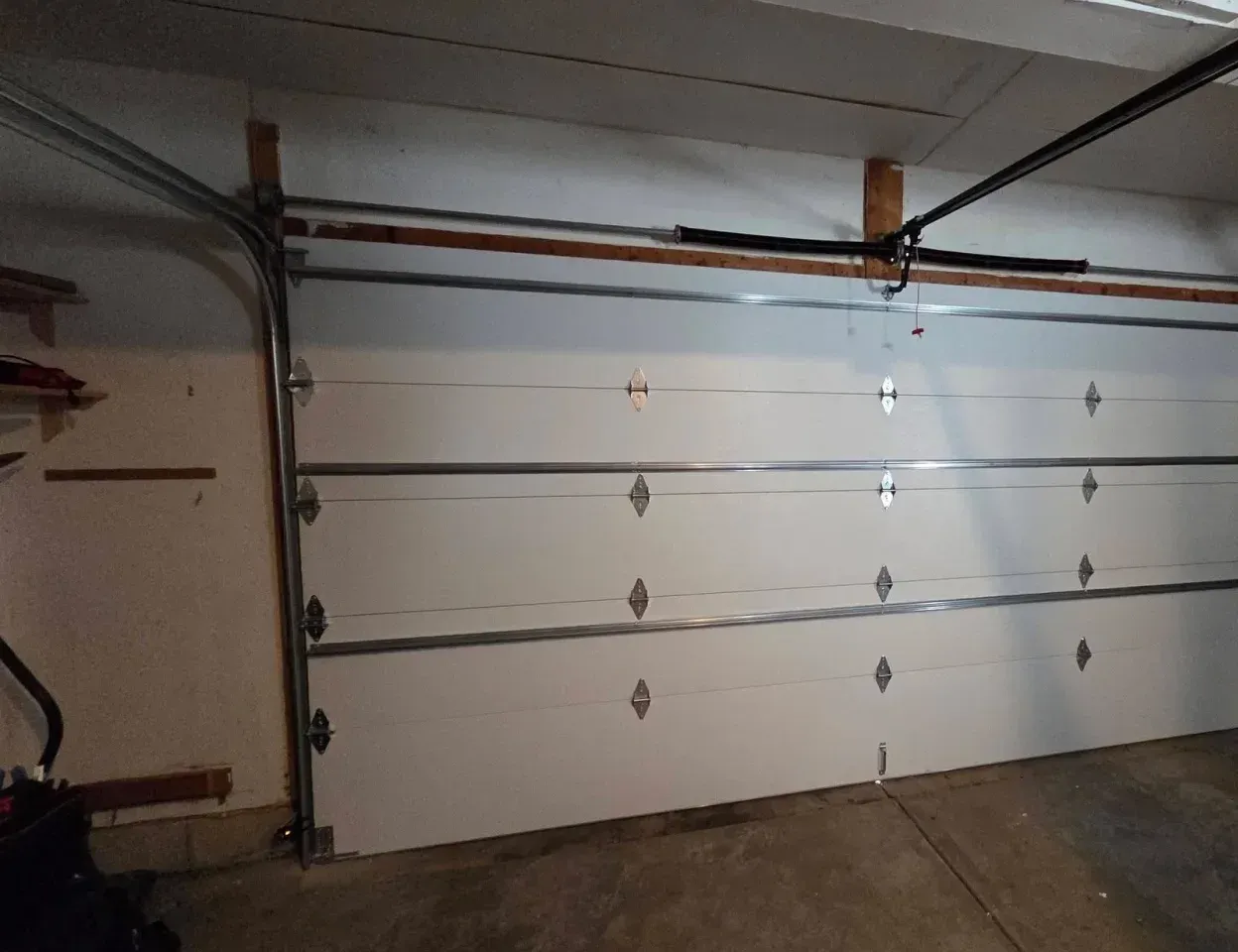 A closed garage door from inside, with its spring and opener rail above