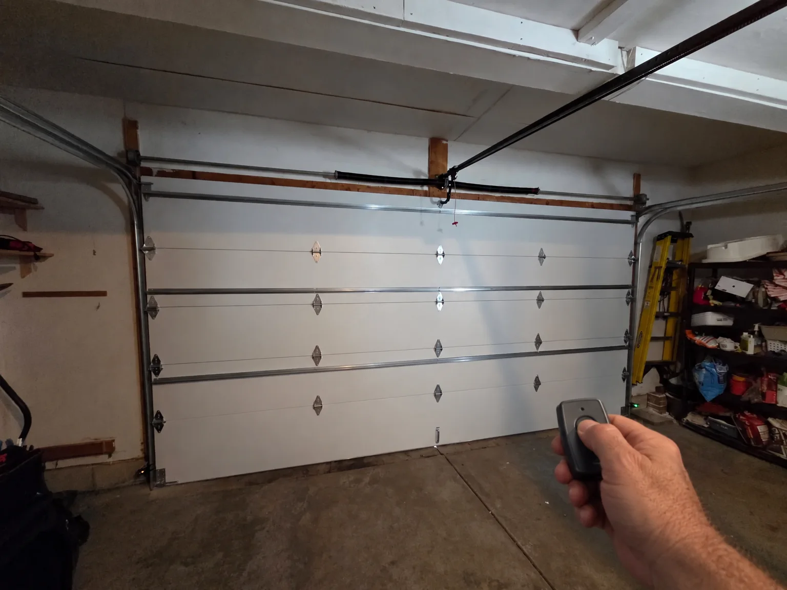 A hand holding a garage door remote, pressing the button, with the closed door beyond