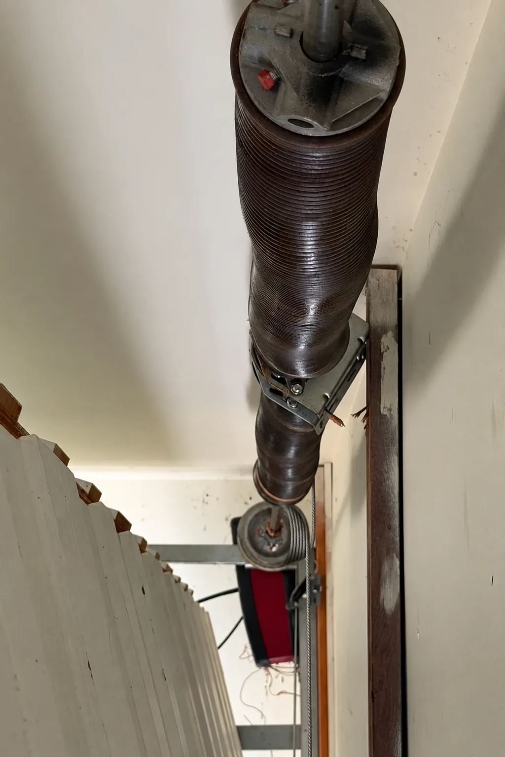 The cable drum at the end of a garage door's spring shaft, its lift cable wound in the grooves