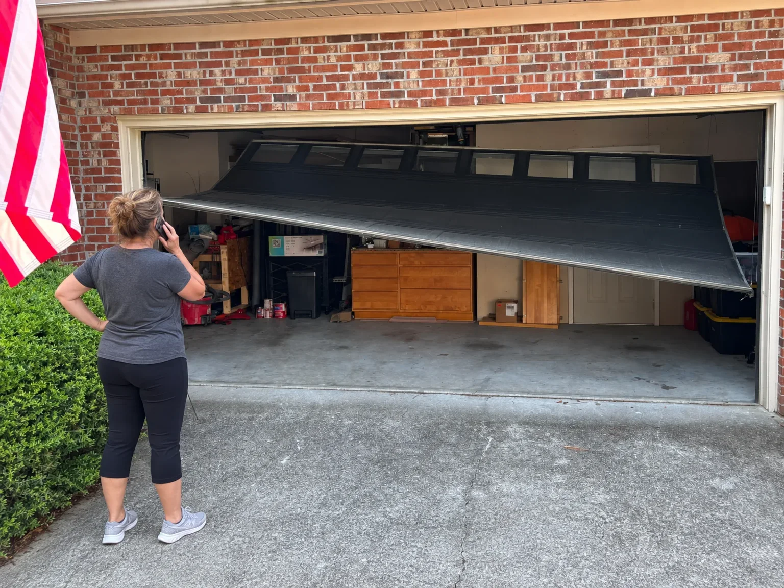 A homeowner on the phone looking at a garage door hanging crooked