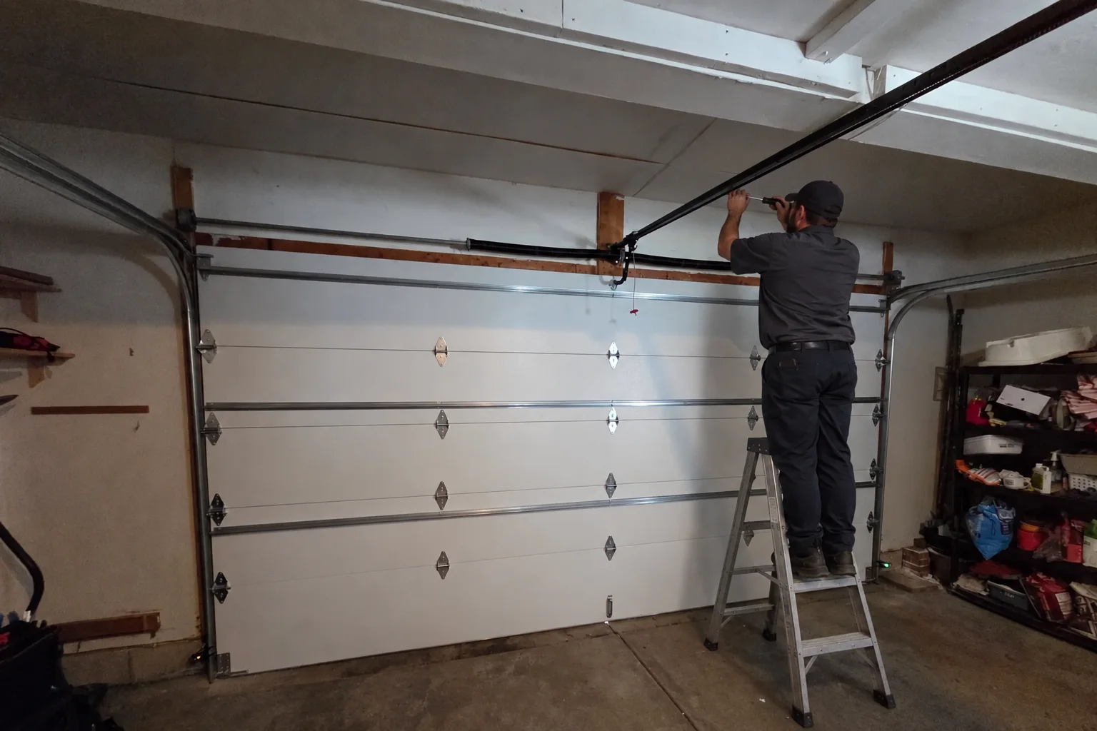 A technician on a ladder working on a garage door opener rail