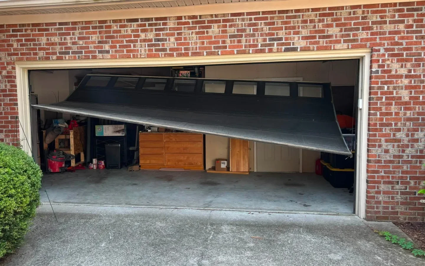 A garage door hanging crooked out of its track on a brick house