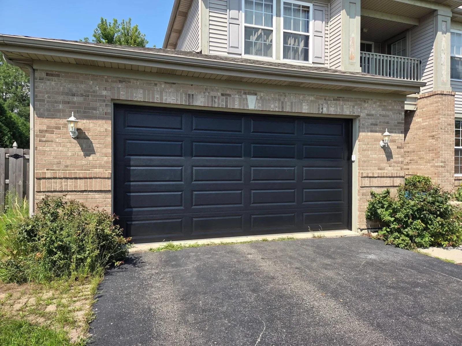 A black raised-panel garage door on a brick house