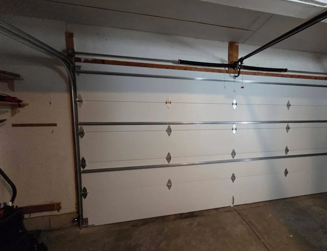 A closed garage door from inside, with its spring and opener rail above