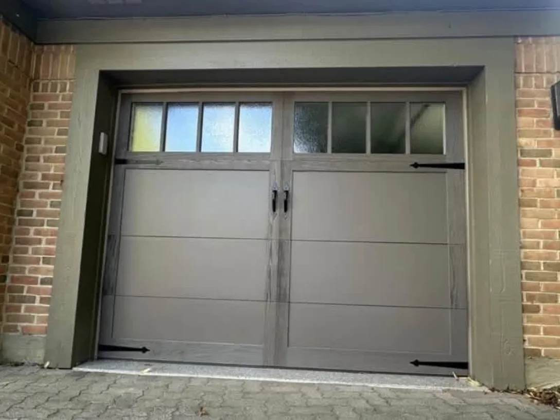 A gray carriage-style garage door on brick